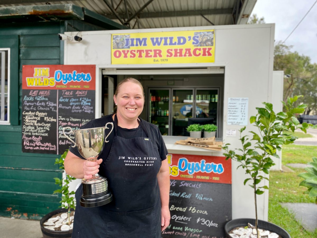 Sally holds a trophy and smiles in front of the Jim Wild's Oyster Shack counter.