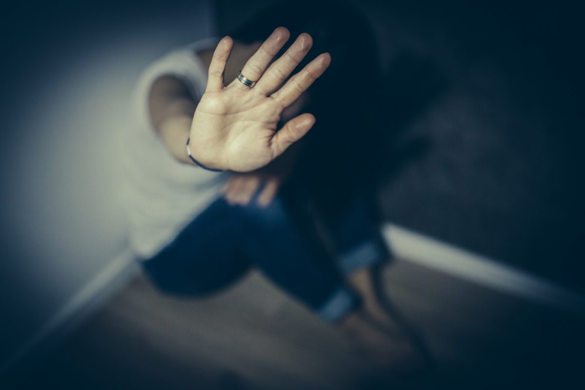 An abused woman sits on floor and holds her hand out in a stop gesture