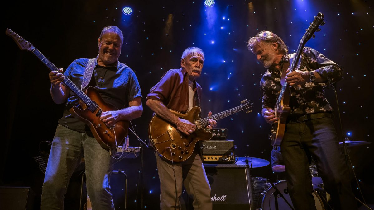Three members of Kings of The Blues with guitars on stage
