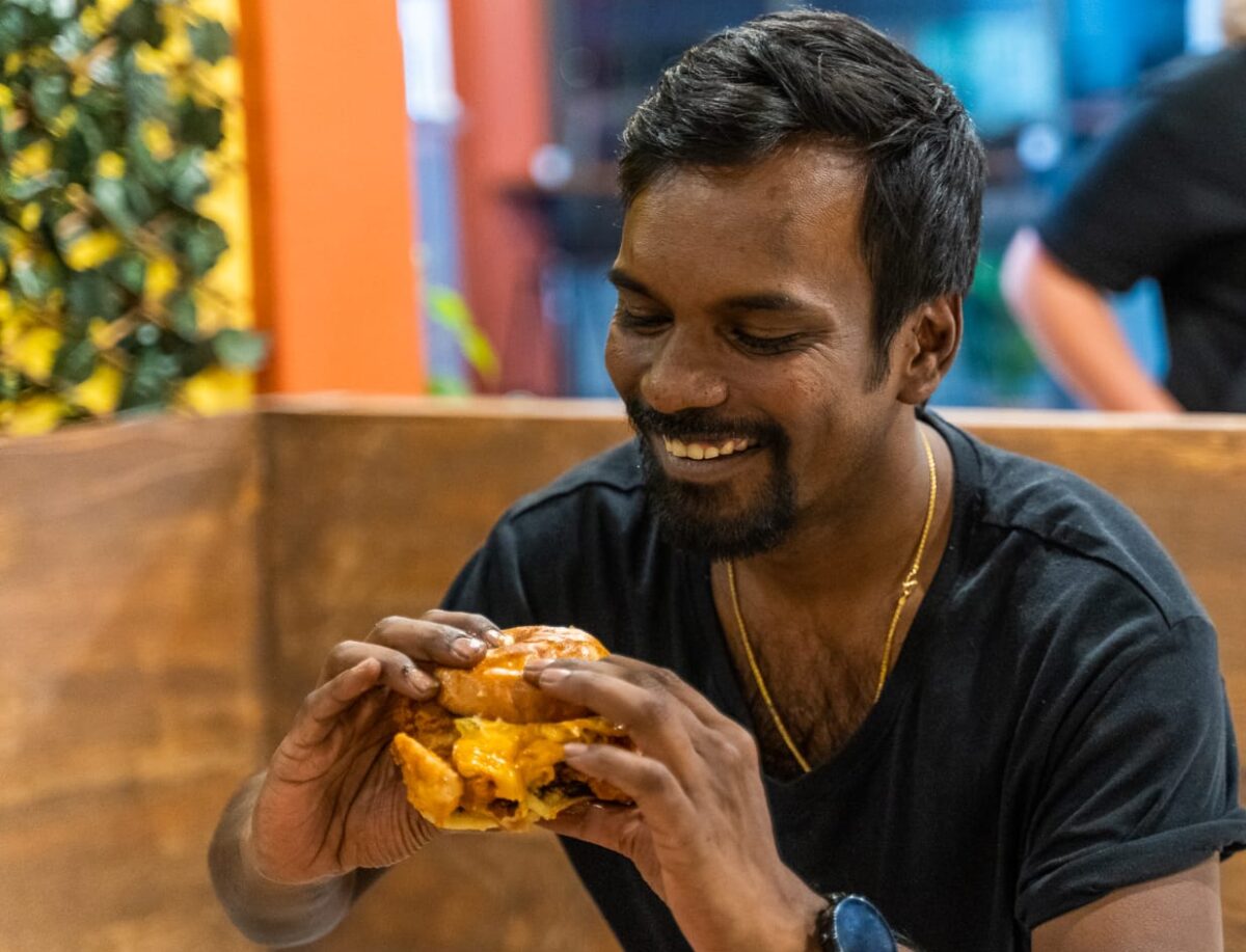 Goutham holding a chicken burger and smiling