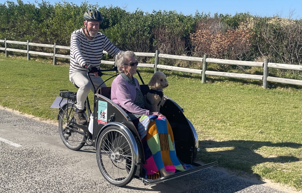 Cycling Without Age President Paul Taylor guiding Judy Young and her dog Charlie on a trishaw ride