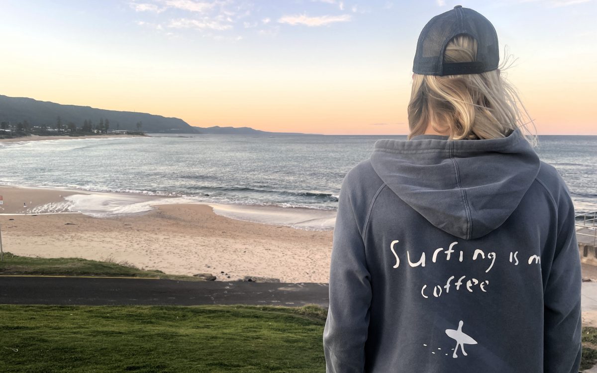 Cooper Palmer facing Woonona Beach in "Surfing Is My Coffee" hoodie.