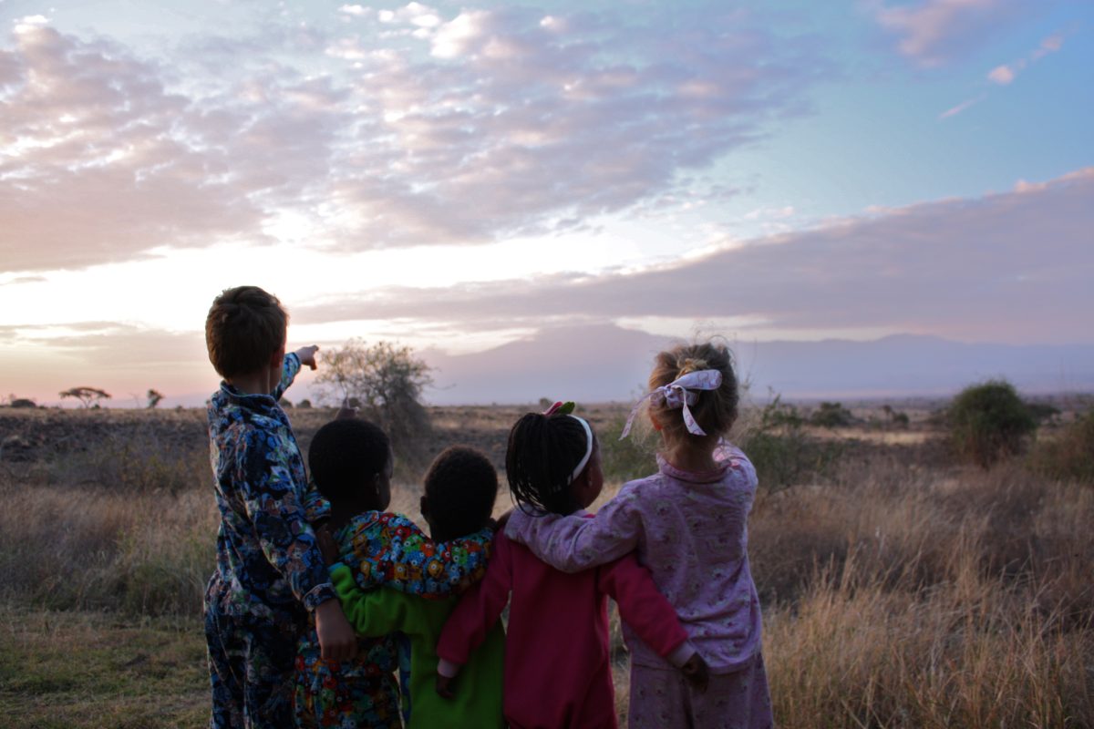 Five children in their pyjamas photographed from behind looking out at a Tanzanian landscape
