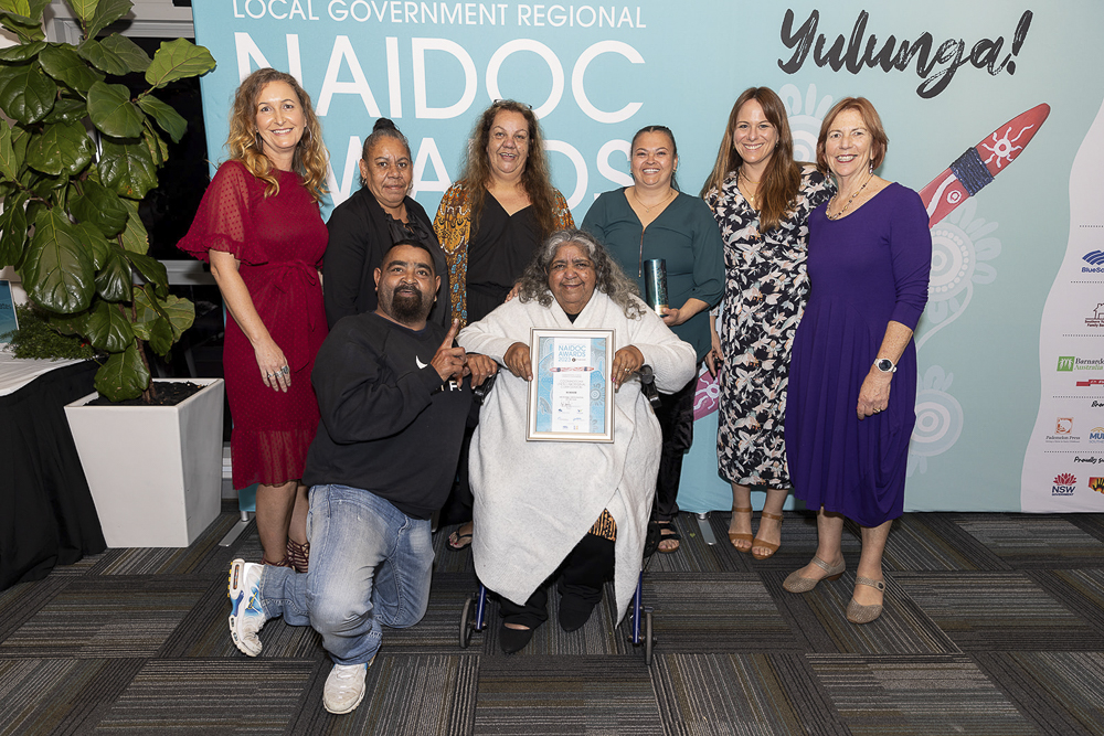 Eight people from the Coomaditchie United Aboriginal Corporation pose with an award