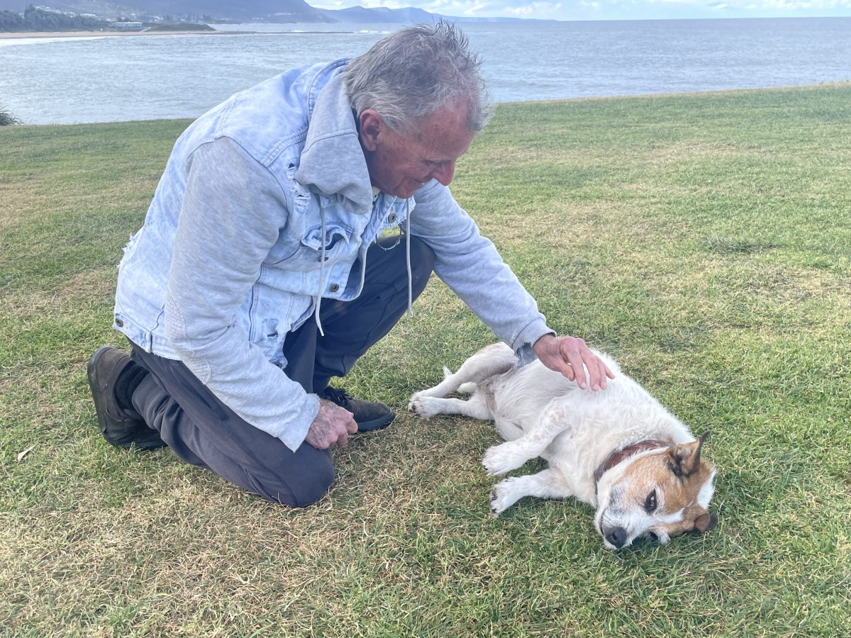 Bill Lenane patting his dog at Bulli Beach. 