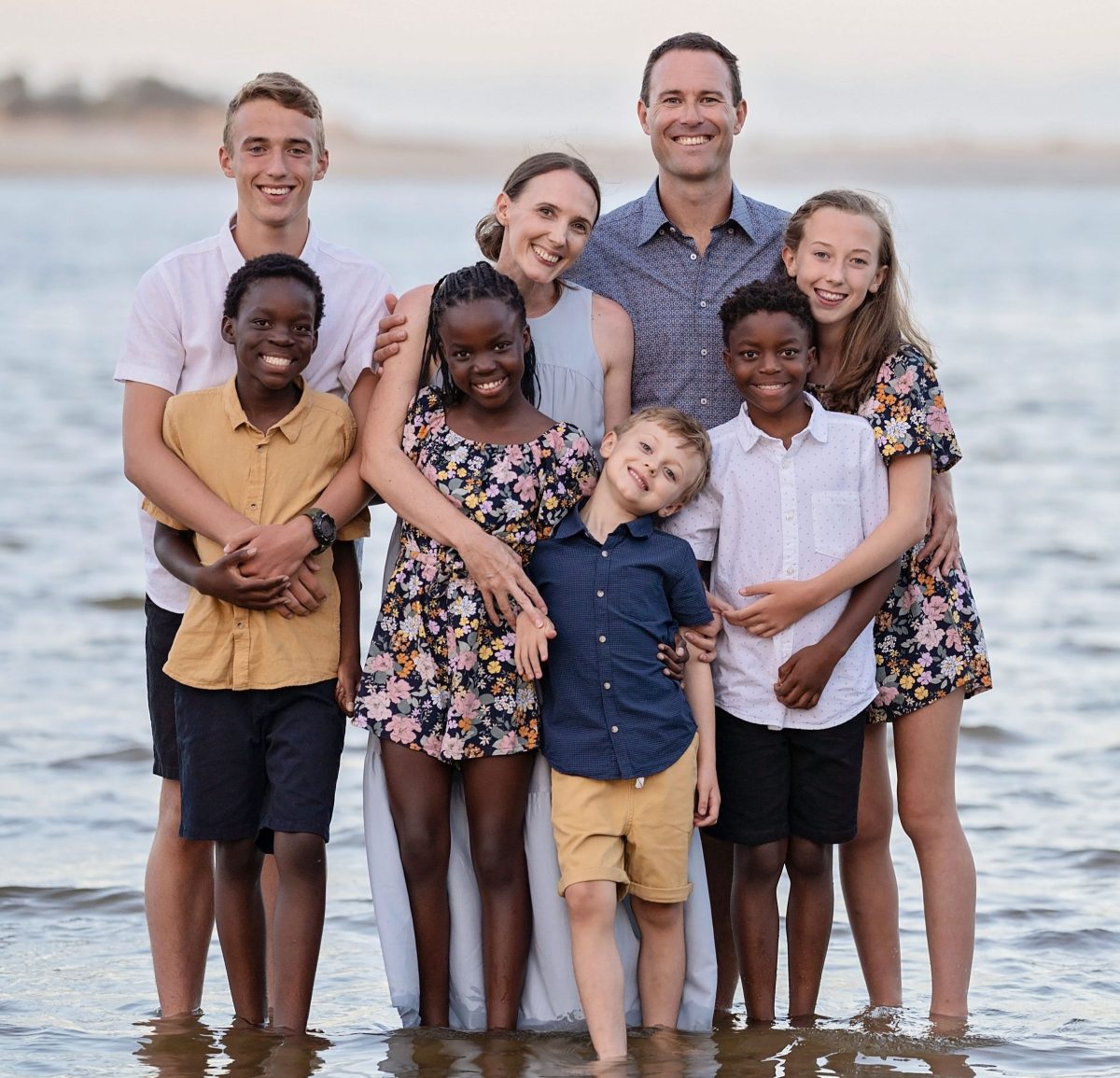 Anna and Mark Dombkins with their three biological children and three adopted children stand on a beach