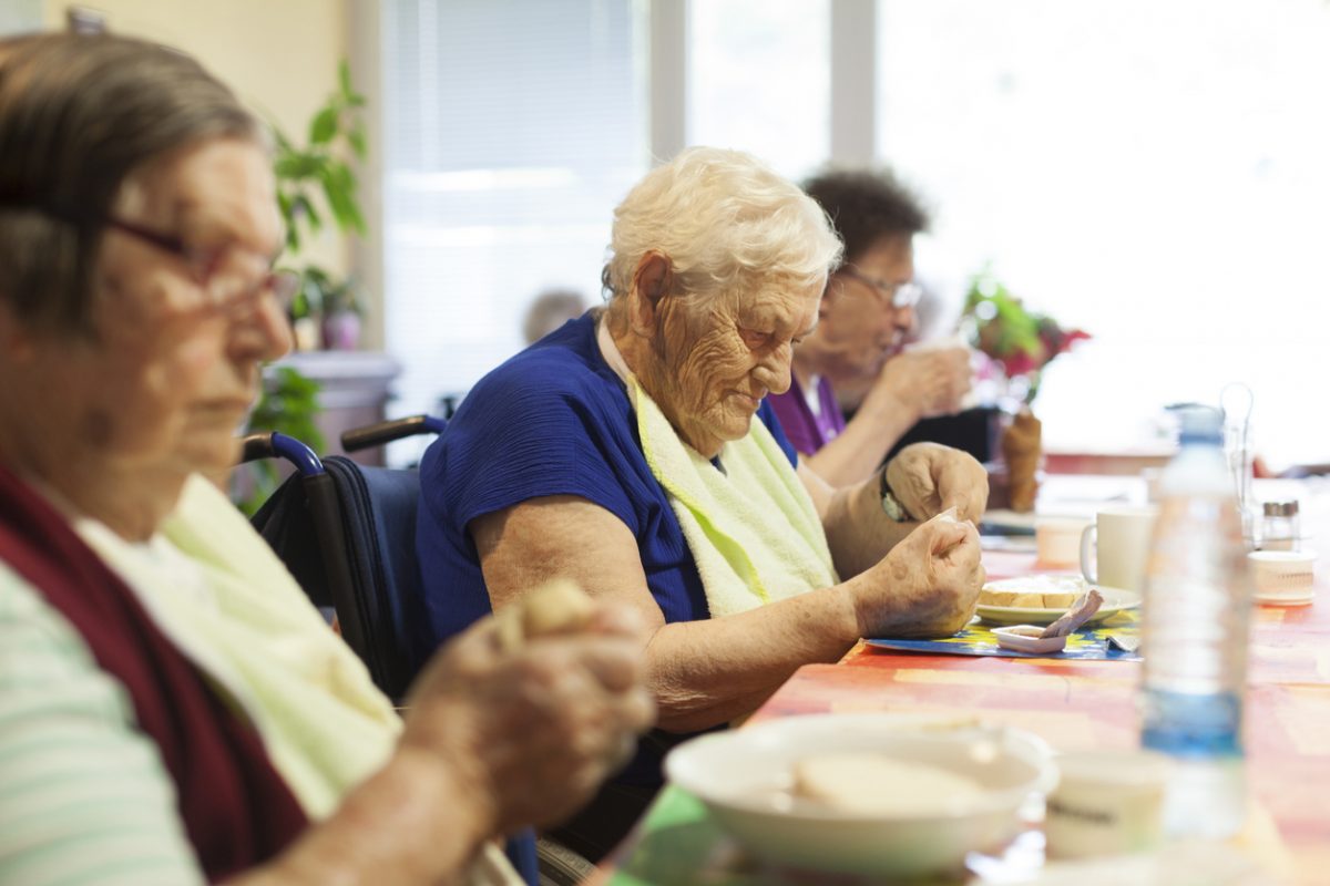 Elderly people eating in dining room aged care facility. 