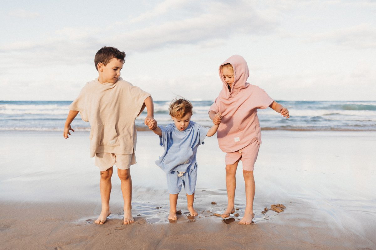 Three children play on the beach in Rugii wearable hooded towel sets
