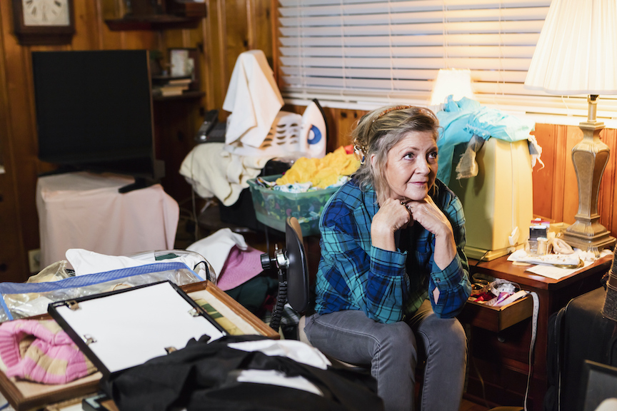 A woman sitting in a messy room.