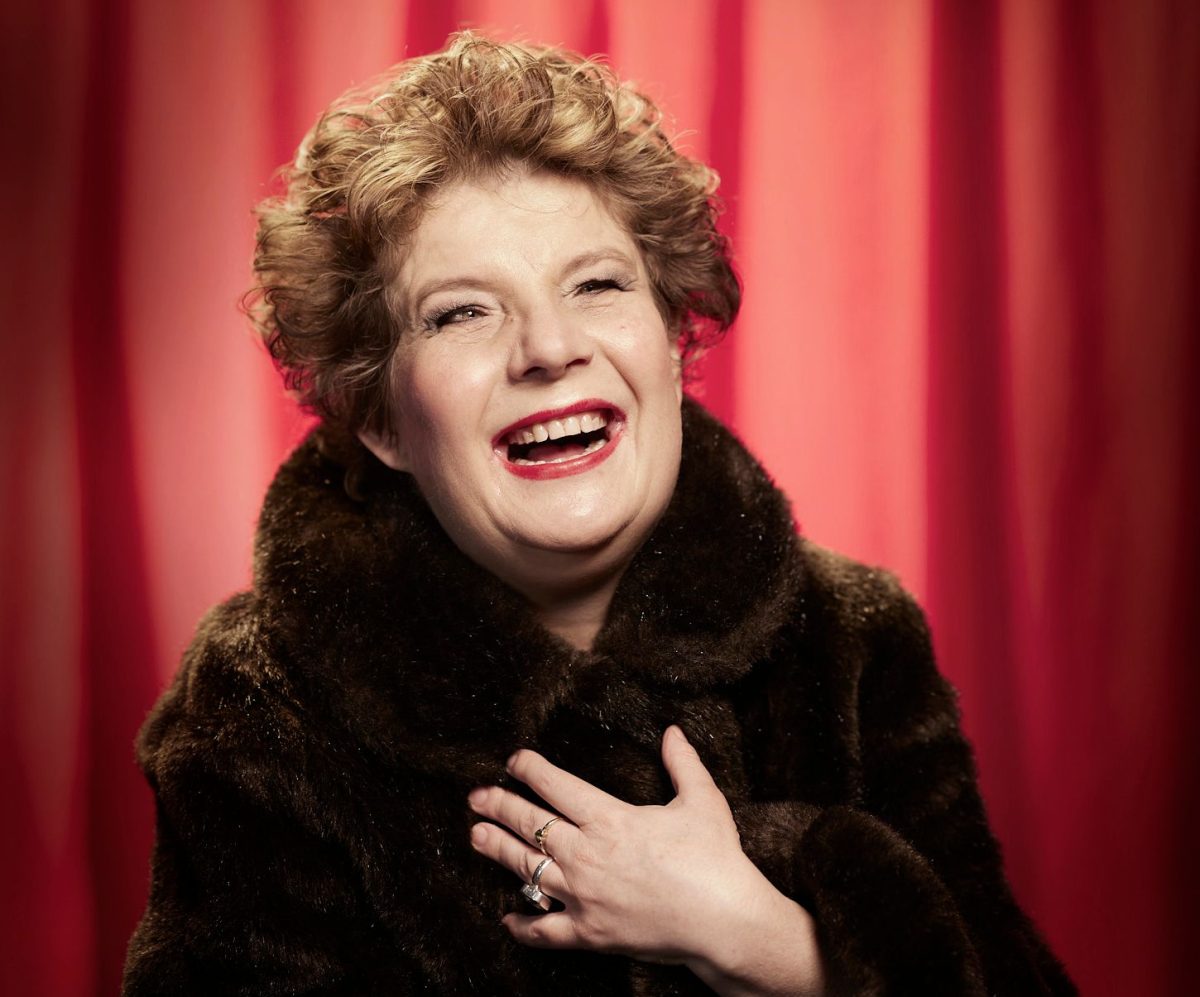 A smiling woman in a fur coat in front of a red curtain