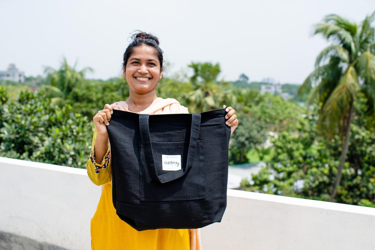 Woman in Bangladesh holds up a black Earth Worthy jute bag