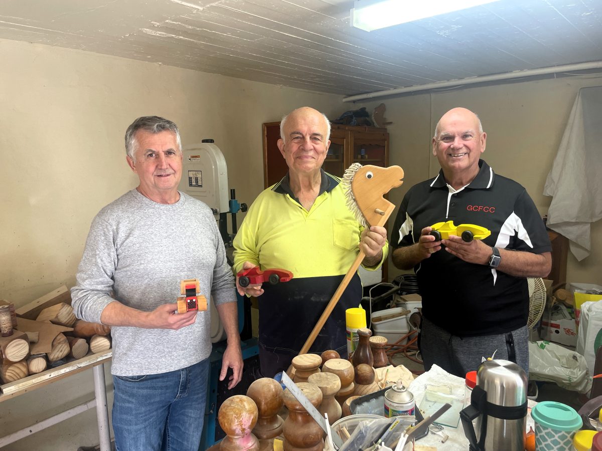 Three men with wooden toys they created in their group's workshop 