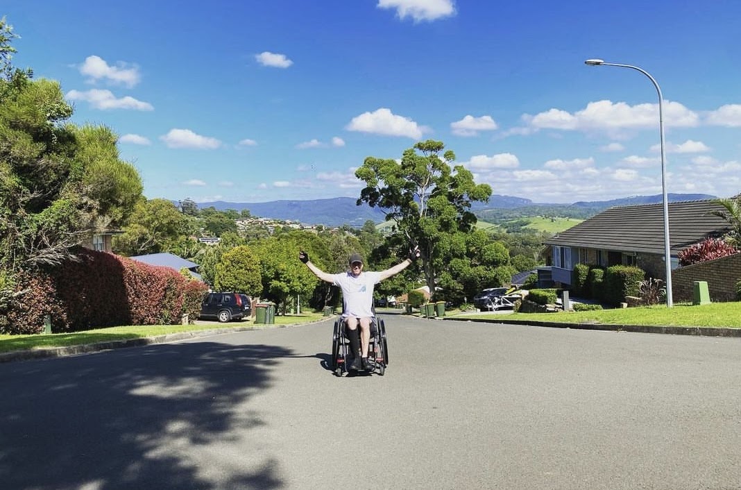 Kiama man Grant Wilson in a wheelchair with his arms raised triumphantly.