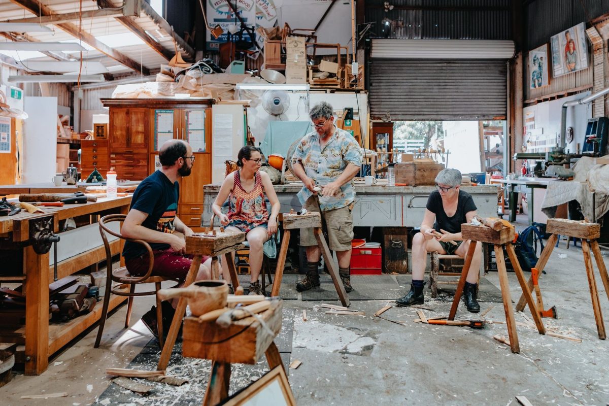 woodworker Brad Van Luyt instructs three people on carving wood in a warehouse
