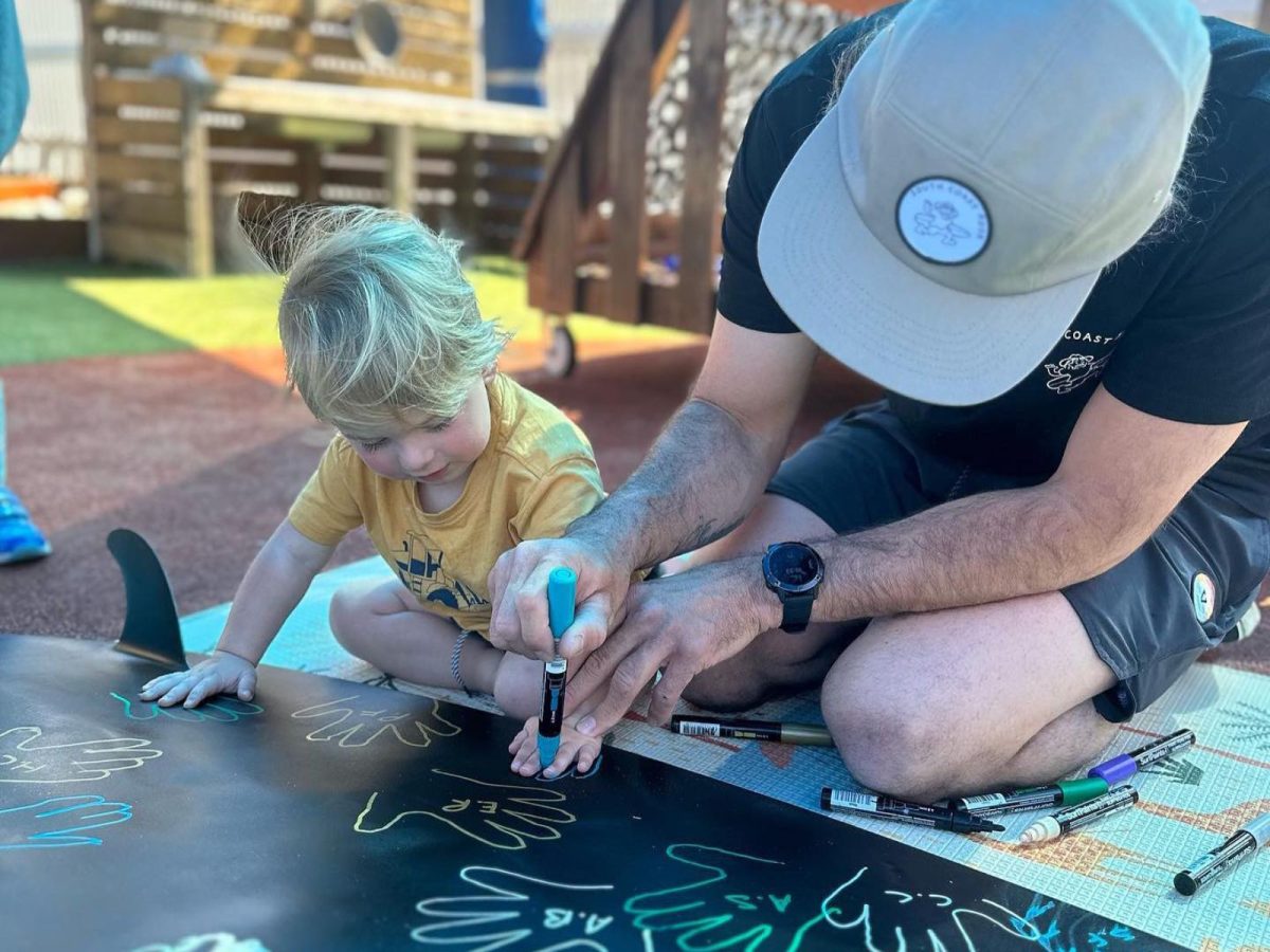 A man and a child drawing with paint pens on a skateboard