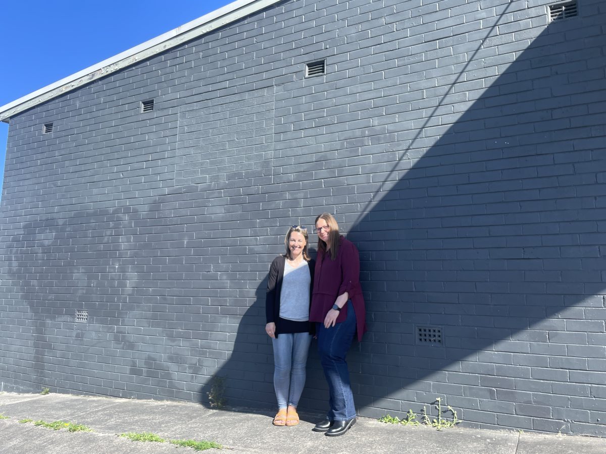 two women standing in front of shop's blank exterior wall