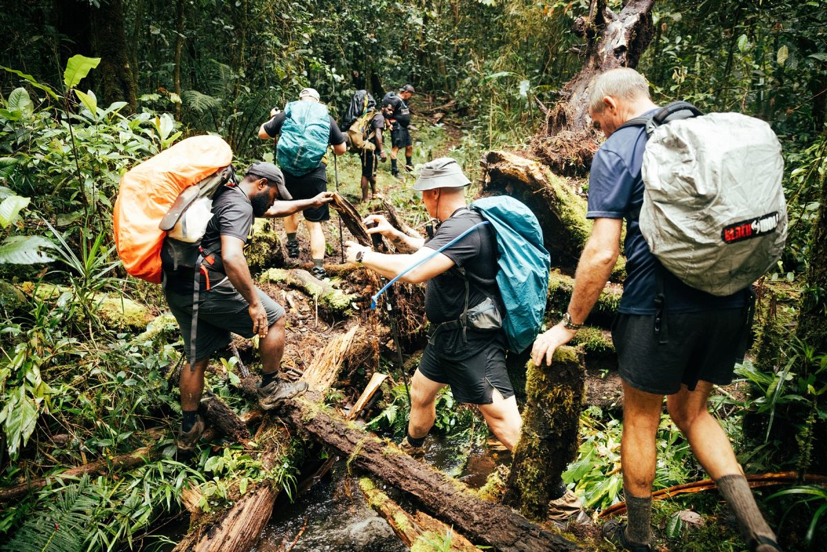Man Walk and Barstool Brothers helping each other over a river on the Kokoda Trail in Papua New Guinea. 