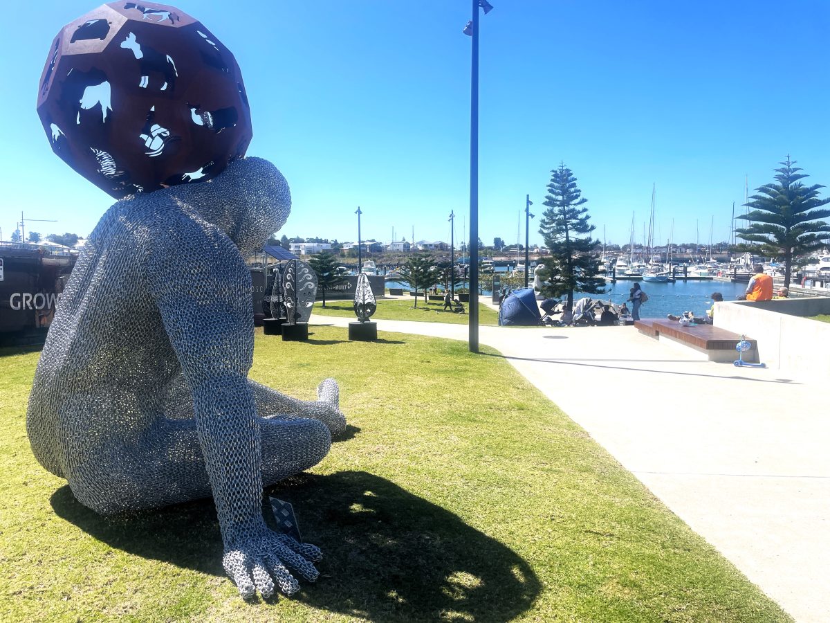 Sculpture of man holding world overlooking marina where people are gathered.