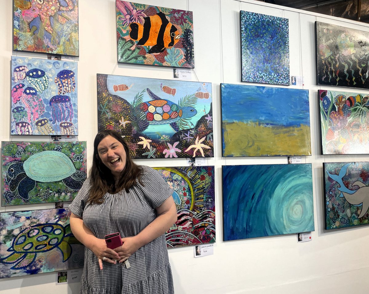 Artist Alexia Waldon beside her jellyfish painting and beneath her fish artwork. 