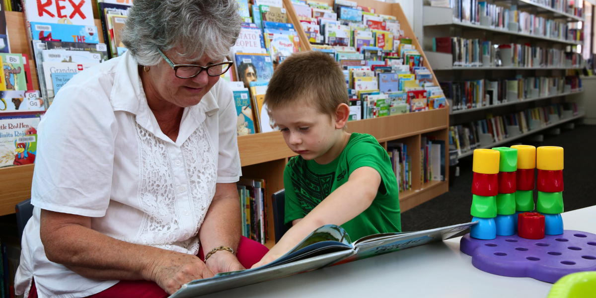 Grandmother reads to her grandson in a library