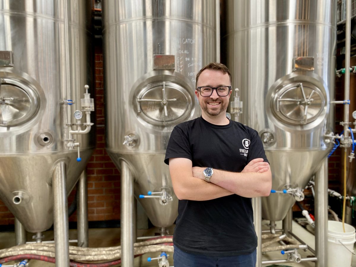 Phil O'Shea stands in front of large beer tanks.