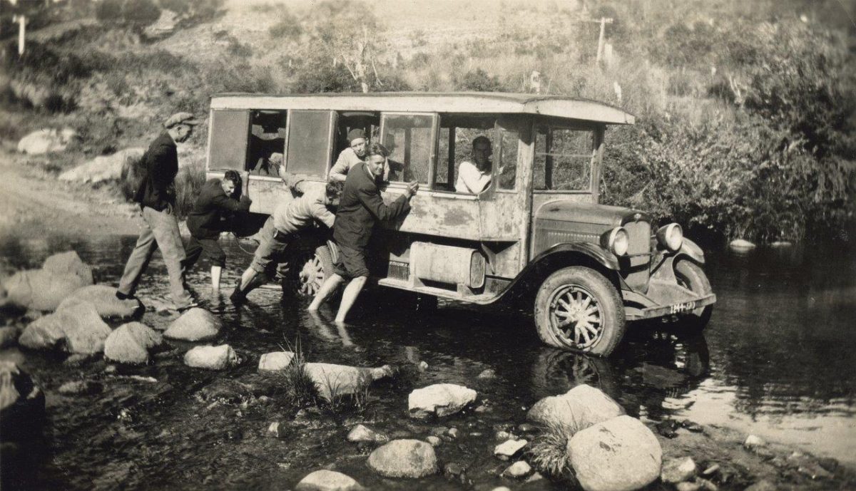 Black and white photo of people pushing an old Dion's Bus through water