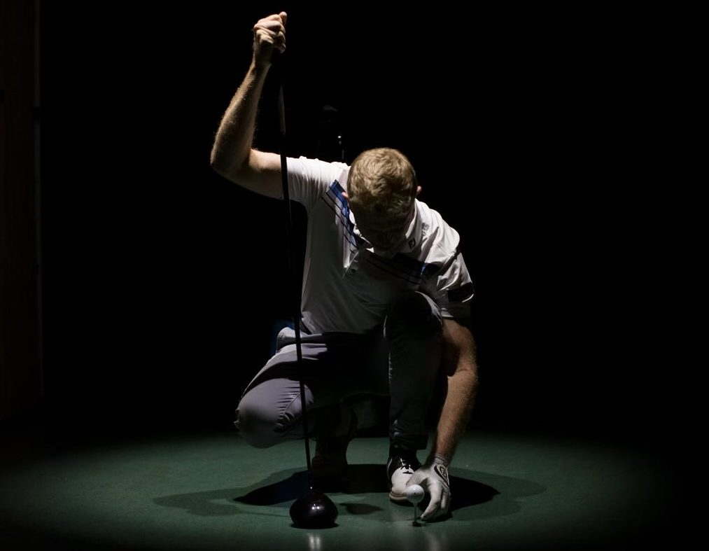 Golfer putting ball down in dark room. 