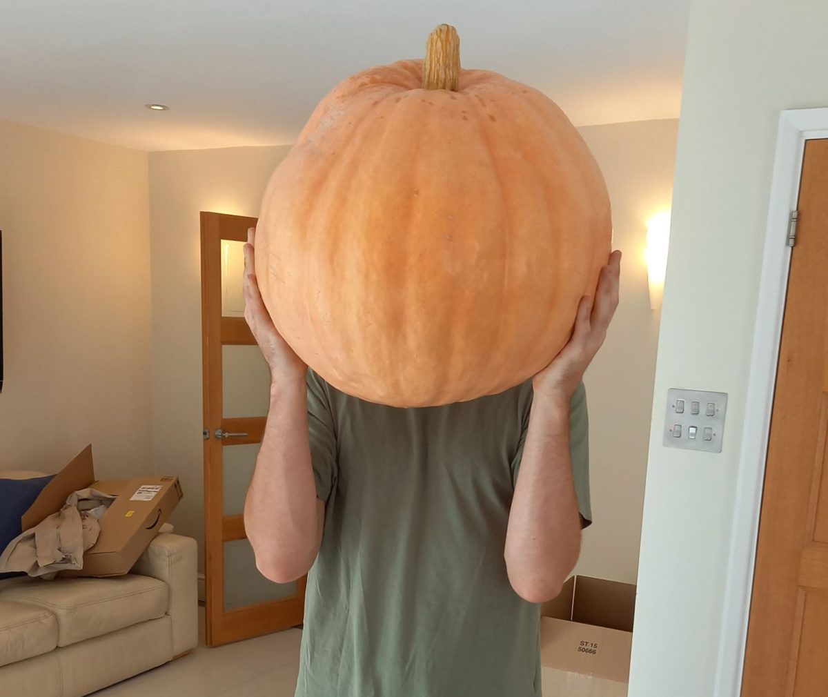 Man holding a giant pumpkin covering his face.