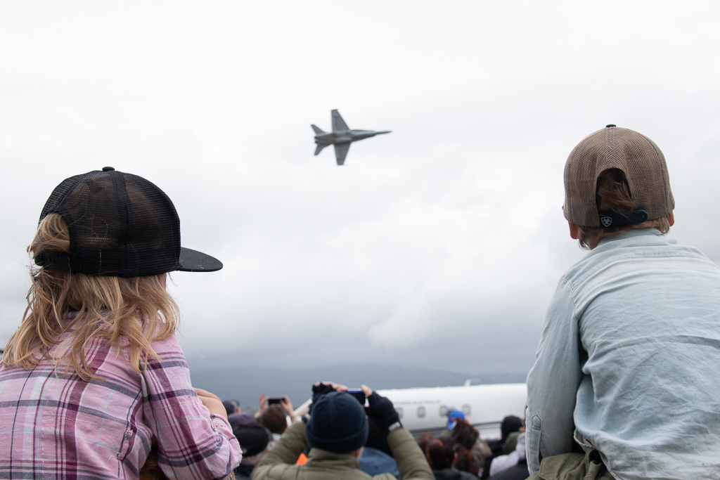 Kids sit on parents' shoulders and watch planes fly