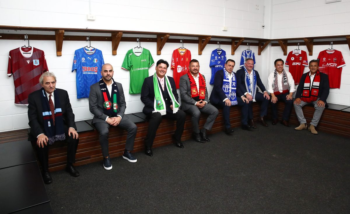 eight men sitting in change room with football jerseys