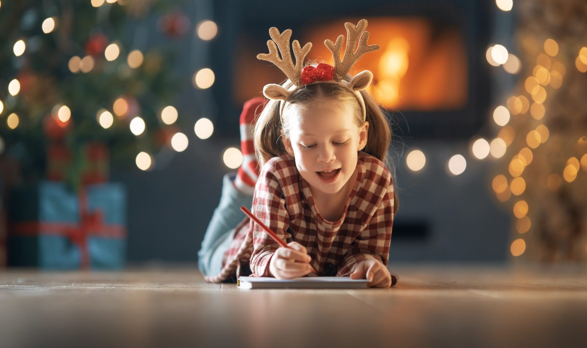 Girl wearing reindeer antlers is writing a letter to Santa