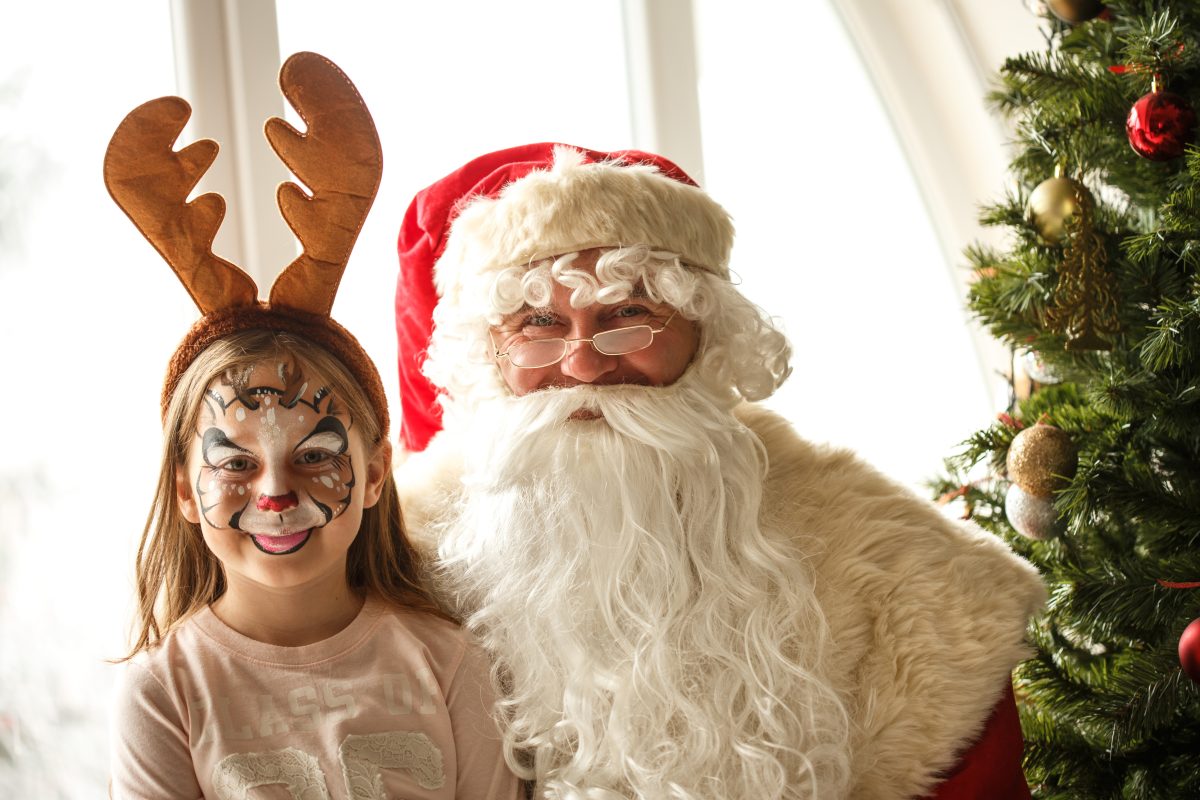Little girl with Reindeer face paint and Santa Claus sitting next to a Christmas tree