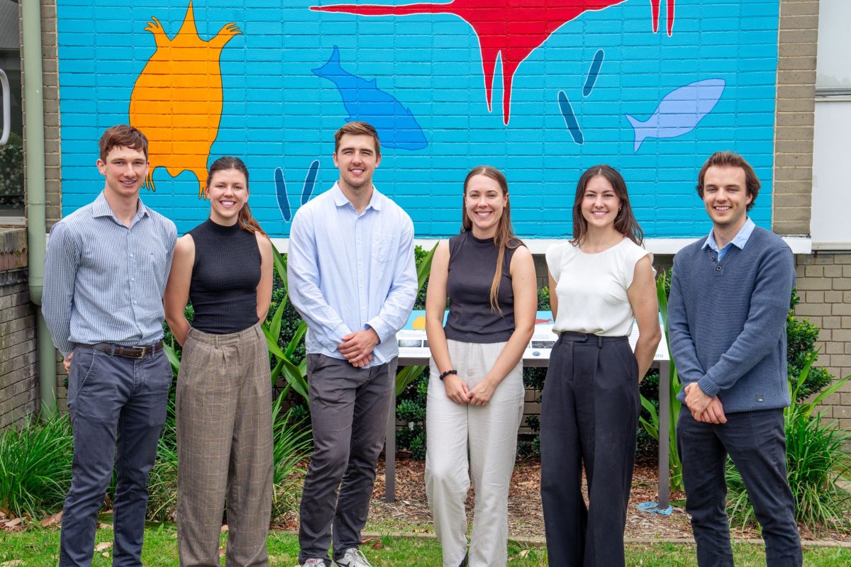 Six students standing in front of a bright mural.
