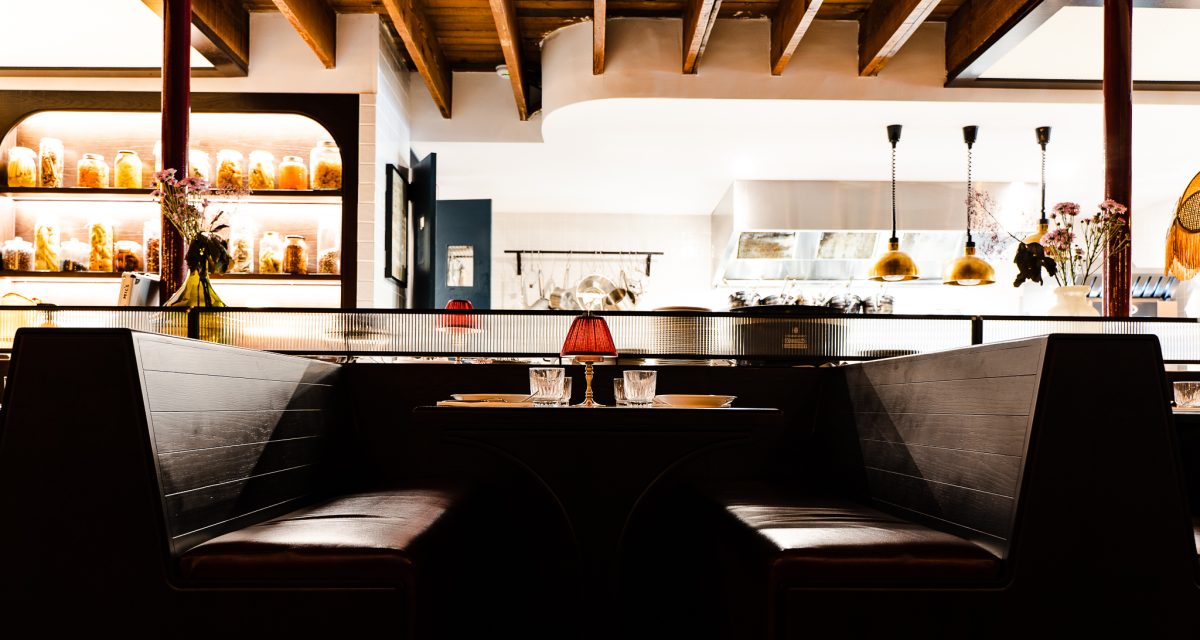 Dark booths with lit up kitchen pass in the background.