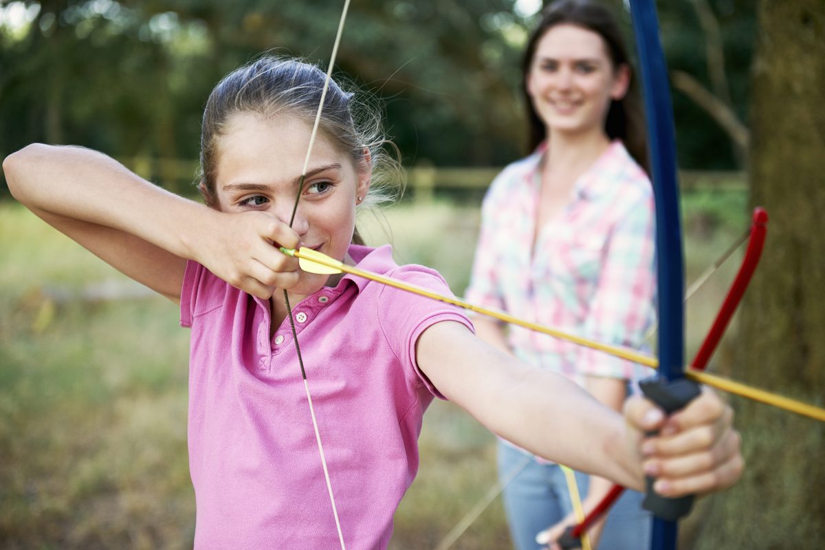 Girl practising archery aiming with bow and arrow