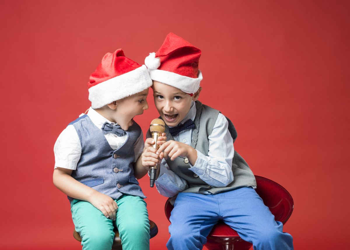 children in christmas hats singing into microphone