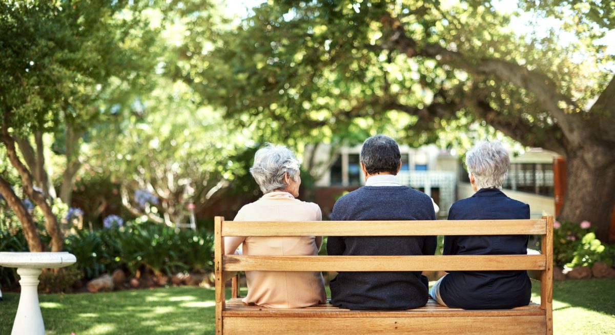 Three older people sitting on a bench in a garden.