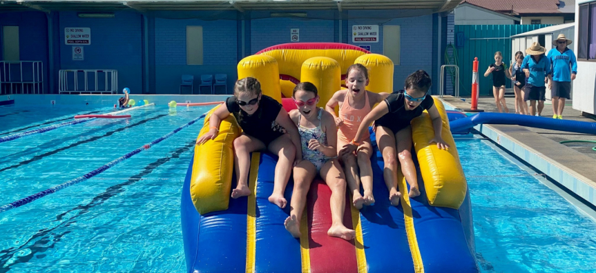 Four kids play on a giant inflatable slide at a Shellharbour pool