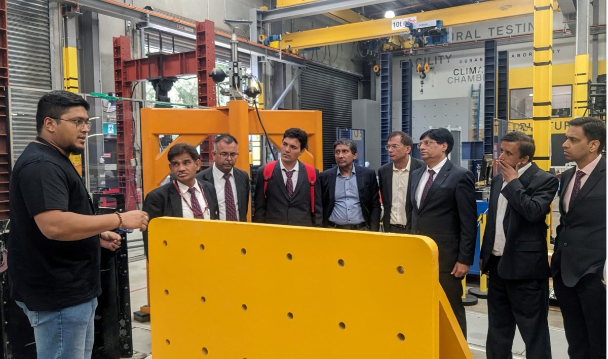 People in suits standing in front of rail equipment at a lab in UTS as a researcher presents