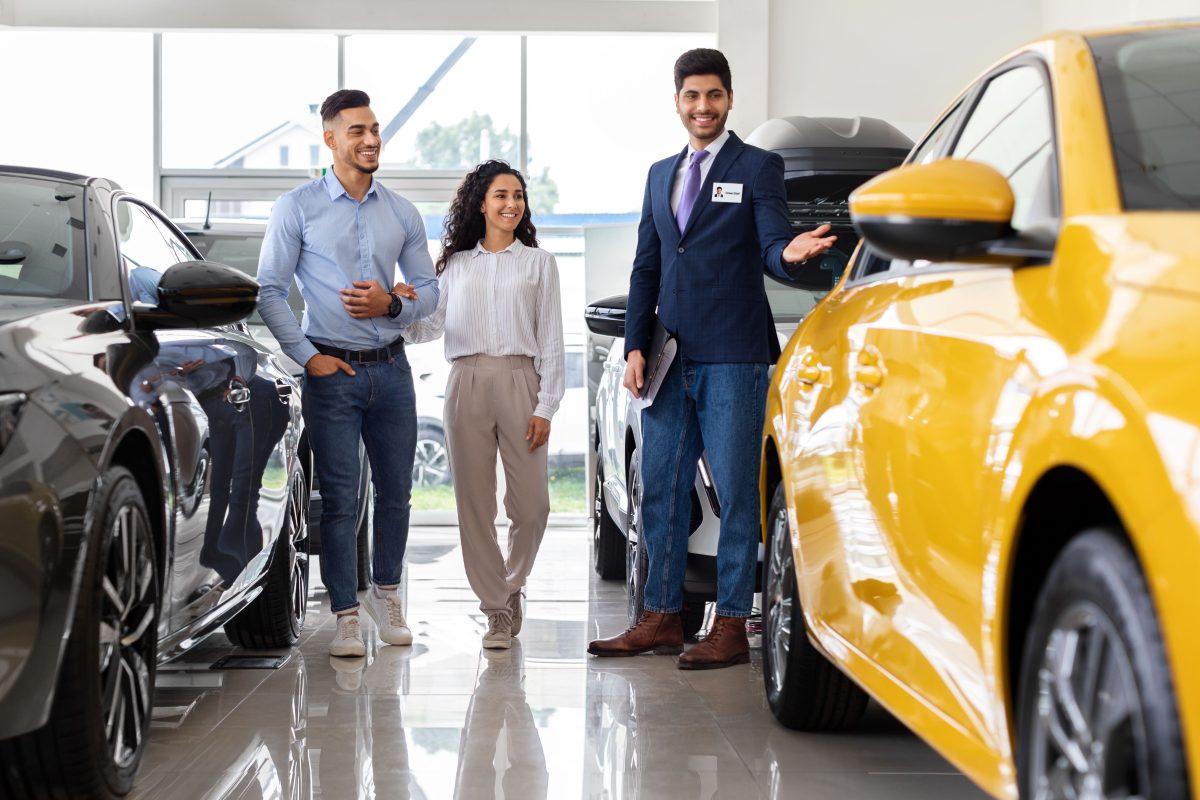 car dealer showing couple yellow vehicle