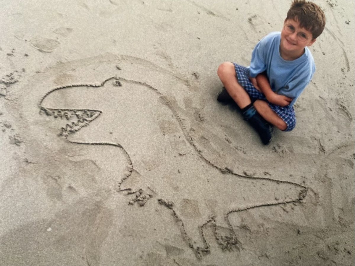 Nathan on beach with outline of dinosaur he drew.
