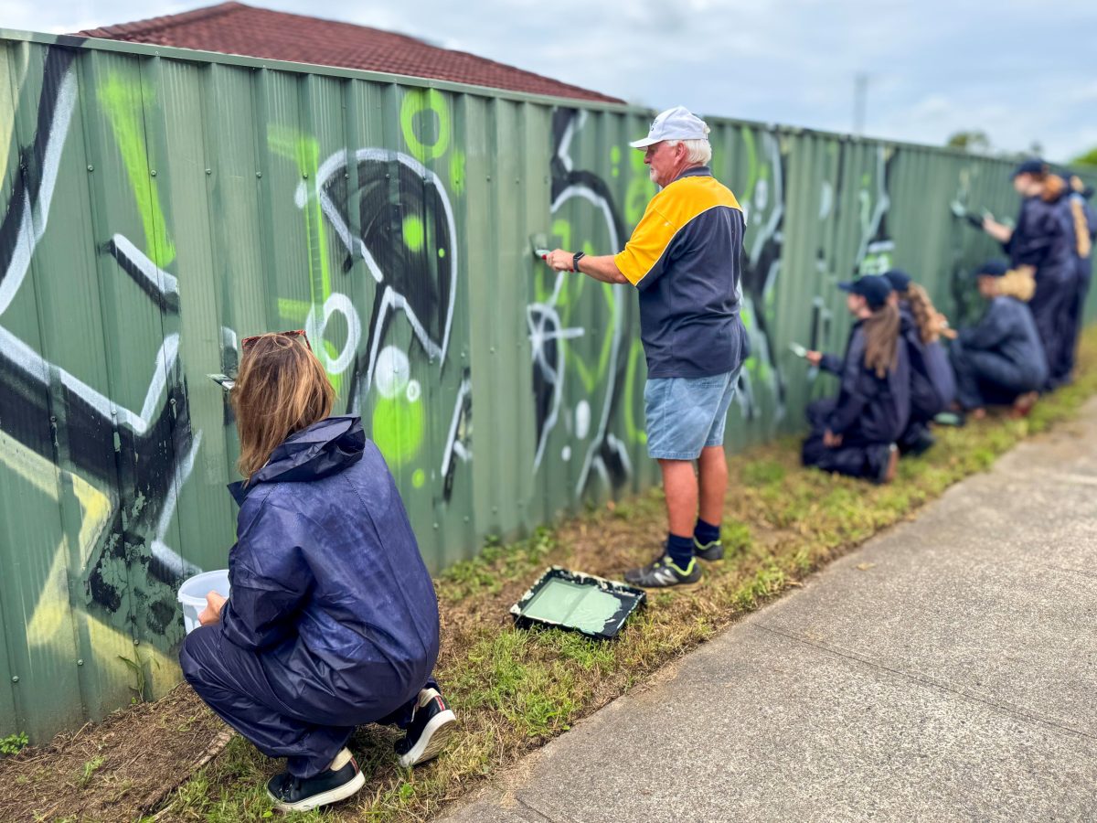 People painting over graffiti on a fence.
