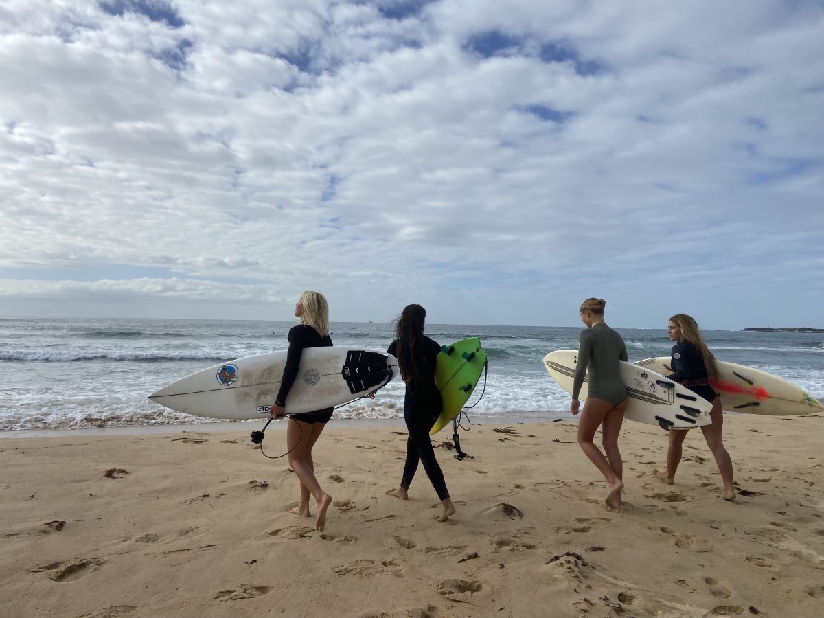 four women walking to the surf with thier boards