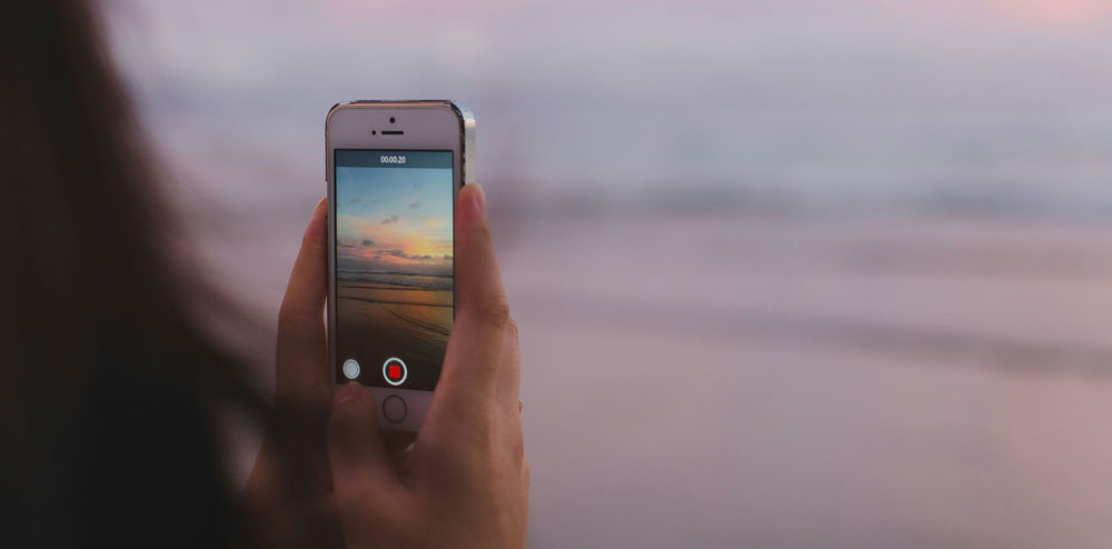 Close-up of hand filming video of ocean on iPhone