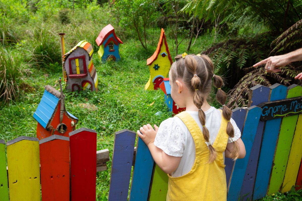 Child looks at colourfully painted fairy houses