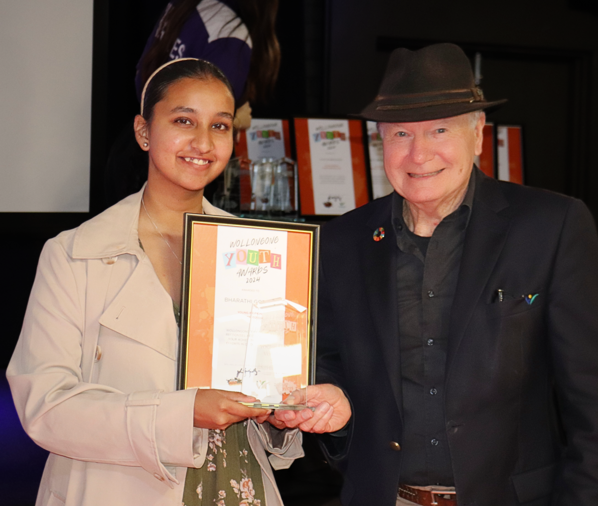 Girl holding an award with man in hat.