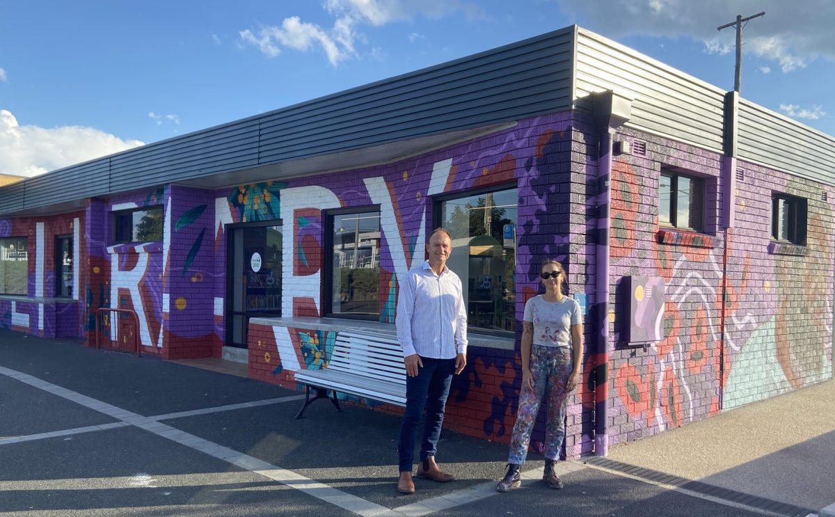 Two people standing in front of a mural on a wall.