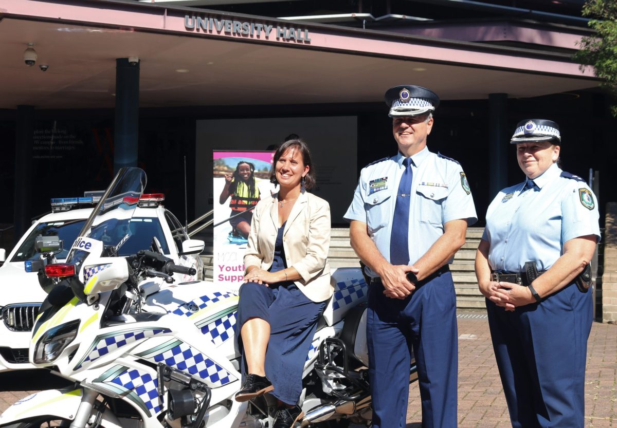Two police officers and a woman sitting on a police bike.