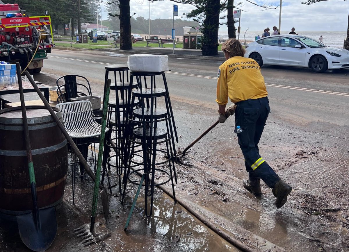 NSW Rural Fire Service member sweeps mud from the front of Shells Austinmer after the floods on Saturday 6 April 2024