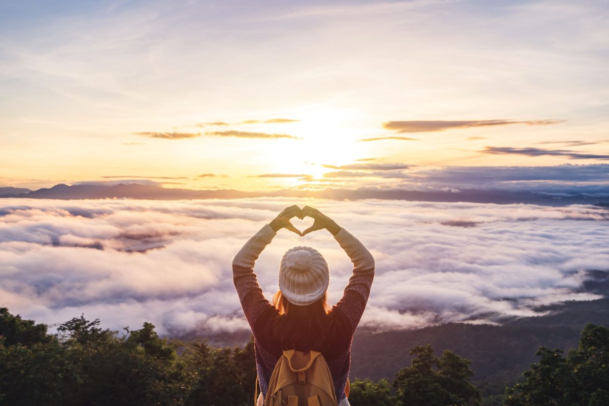 Woman holding up heart sign on top of mountain